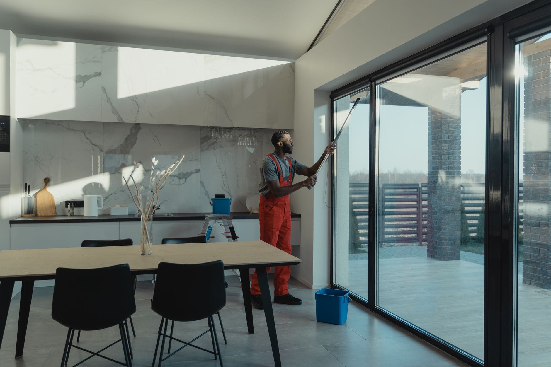 A professional cleaner in uniform washing large glass windows indoors with natural light streaming in. — Corona del Mar real