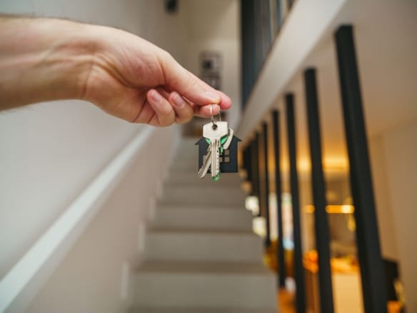 A hand holding house keys in a modern interior, symbolizing new home ownership or real estate investment. — Top of the World