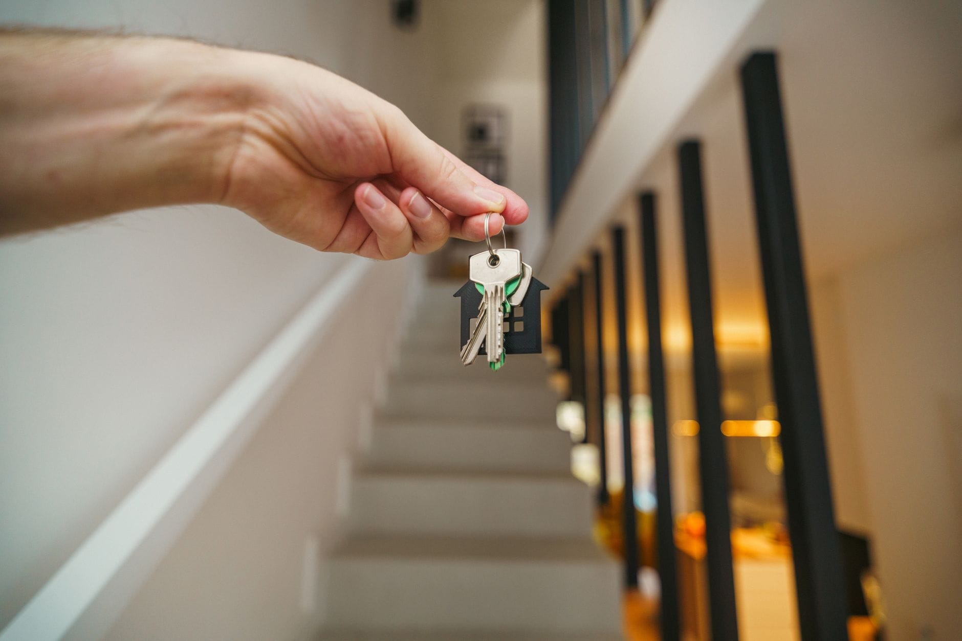 A hand holding house keys in a modern interior, symbolizing new home ownership or real estate investment. — Top of the World